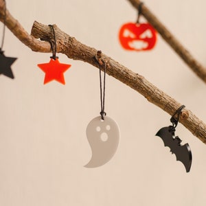 May include: A branch with five Halloween-themed decorations hanging from it. The decorations are a black star, a red star, a white ghost, a black bat, and an orange pumpkin.