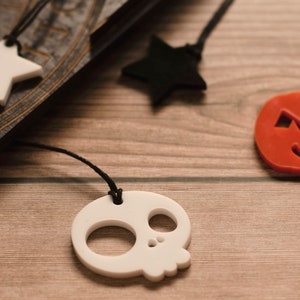 May include: Four Halloween-themed charms on black cords. The charms are a white star, a black star, a white skull, and an orange pumpkin with a jack-o'-lantern face.