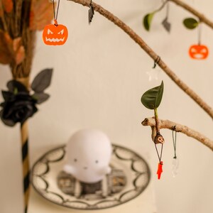 May include: A branch with leaves decorated with Halloween-themed ornaments, including a ghost, pumpkins, and a red lightning bolt.