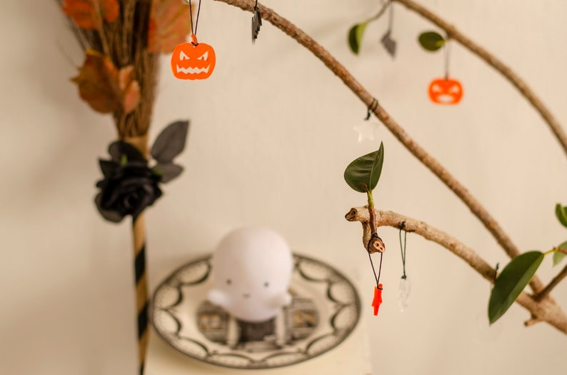 May include: A branch with leaves decorated with Halloween-themed ornaments, including a ghost, pumpkins, and a red lightning bolt.