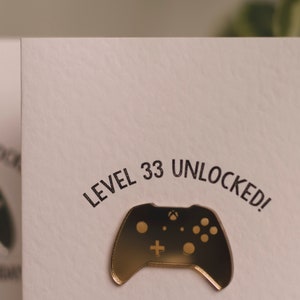 May include: A white card with the text "LEVEL 33 UNLOCKED!" in black lettering. A gold-colored video game controller is on the card.
