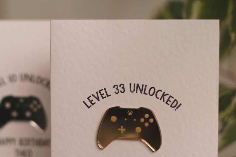 May include: A white card with the text "LEVEL 33 UNLOCKED!" in black lettering. A gold-colored video game controller is on the card.