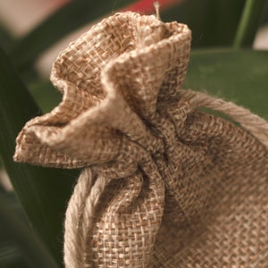 May include: A small, brown burlap drawstring bag with a gathered top. The bag is made of natural fibers and has a rustic, handmade look.