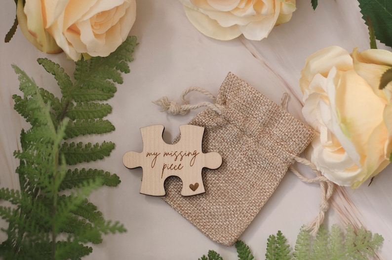 May include: A wooden puzzle piece in the shape of a heart with the text "my missing piece" and a small heart symbol. The puzzle piece is in a small burlap bag with a drawstring.