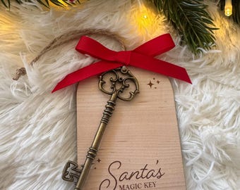 May include: A wooden Christmas ornament with a vintage-style key and a red ribbon. The ornament reads "Santa's Magic Key" and is personalized with names. Festive holiday decor.