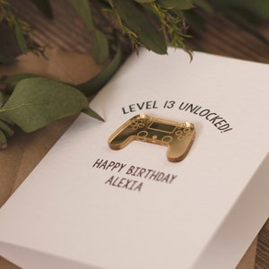 May include: A white card with the text "Level 13 Unlocked!" and a gold-colored video game controller. The card also says "Happy Birthday Alexia".