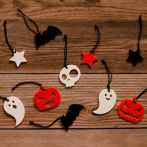 May include: A collection of Halloween-themed decorations, including ghosts, bats, pumpkins, stars, and a skull, hanging from strings on a wooden background.