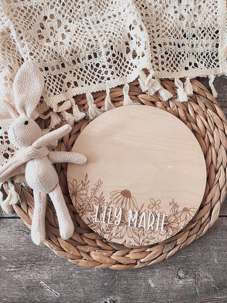 May include: A round wooden sign with a floral design and the name "Lily Marie" engraved in white lettering.