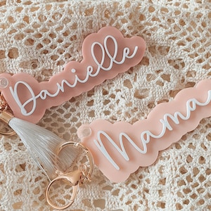 May include: Two pink acrylic keychain charms with white lettering. The top charm says "Danielle" and the bottom charm says "Mama".