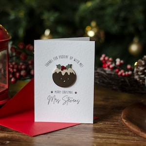 May include: A white Christmas card with a brown and white pudding illustration. The card says "Thanks for puddin' up with me! Merry Christmas" and is signed "Mrs. Stevens".