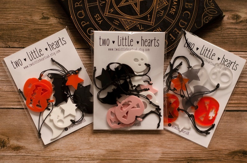 May include: Three packs of Halloween decorations. Each pack contains a variety of cut-out shapes, including pumpkins, bats, ghosts, and stars. The shapes are made of different colours, including orange, black, white, and pink. The packs are labelled "two little hearts" and include the website address www.twolittleheartsuk.etsy.com.