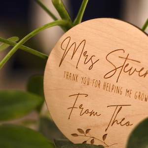 May include: A round wooden sign with the text "Mrs. Stevens Thank you for helping me grow From Theo" and a small leafy design.