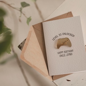 May include: A white card with the text "Level 33 Unlocked!" and a gold-colored video game controller icon. Below the text is "Happy Birthday Uncle Jimbo". The card is in a brown envelope.