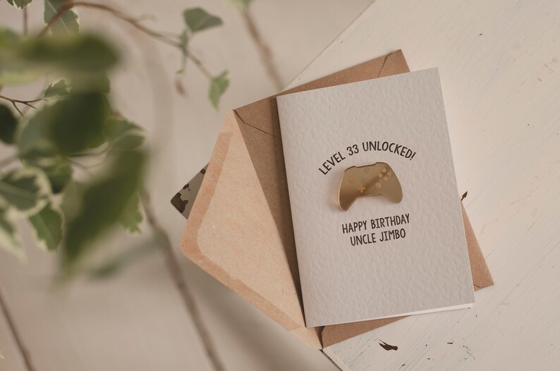 May include: A white card with the text "Level 33 Unlocked!" and a gold-colored video game controller icon. Below the text is "Happy Birthday Uncle Jimbo". The card is in a brown envelope.