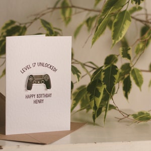 May include: A white card with the text "Level 17 Unlocked!" and a silver video game controller graphic. The text "Happy Birthday Henry" is below the graphic.