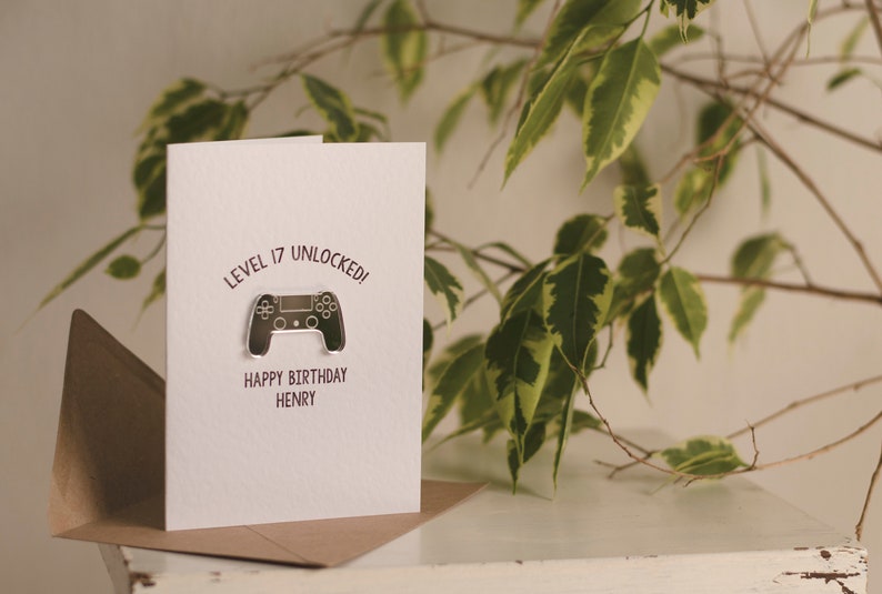 May include: A white card with the text "Level 17 Unlocked!" and a silver video game controller graphic. The text "Happy Birthday Henry" is below the graphic.