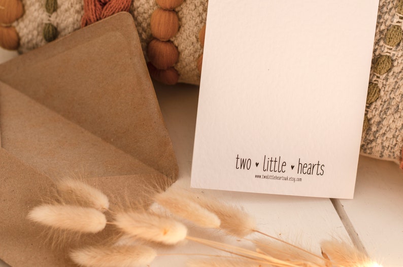 K&ouml;nnte beinhalten: Eine wei&szlig;e Karte mit dem Text "two little hearts" und der Website-Adresse "www.twolittlehearts.etsy.com". Die Karte liegt auf einer Holzoberfl&auml;che mit einem braunen Umschlag und etwas trockenem Gras.
