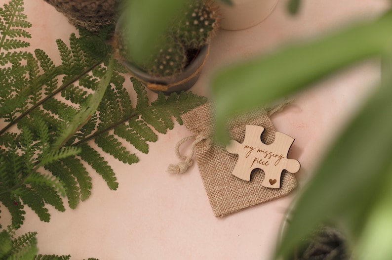 May include: A small wooden puzzle piece in a burlap bag. The puzzle piece is engraved with the words "my missing piece" and a small heart.