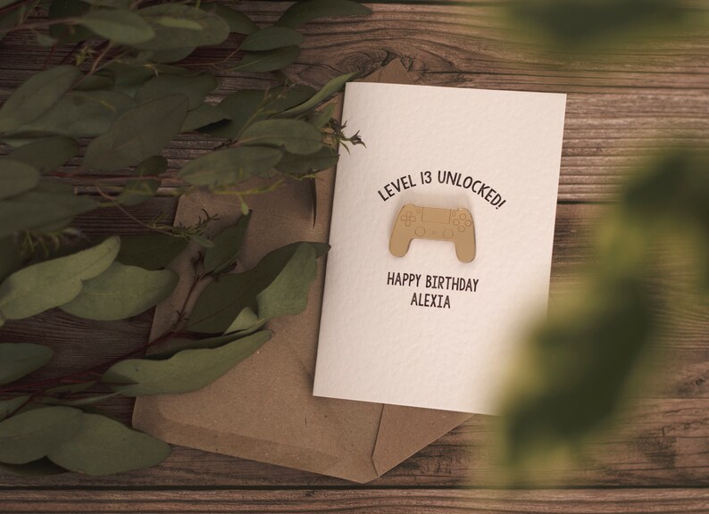 May include: A white card with the text "Level 13 Unlocked!" and a brown video game controller graphic. Below the graphic is the text "Happy Birthday Alexia".