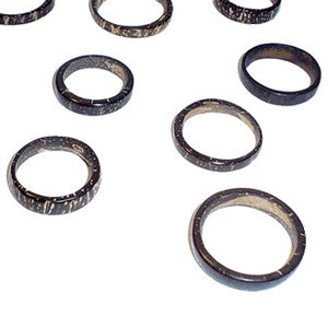 Może przedstawiać: Dziesięć prostych drewnianych pierścieni z czarno-złotym wzorem w kropki. Pierścienie są różnej wielkości i ułożone są w kółko na białym tle.