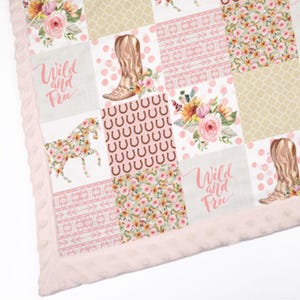 May include: A pink and brown patchwork baby blanket featuring a horse, cowboy boots, horseshoes, and floral designs. The blanket has a pink minky backing and the text "Wild and Free" is featured twice.