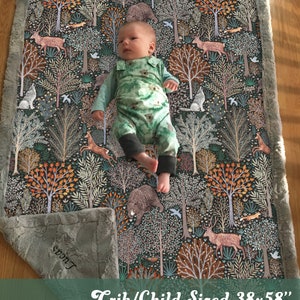May include: A crib-sized baby blanket with a woodland print featuring trees, animals, and birds. The blanket is gray with a soft, fuzzy texture and has a white border. The blanket is 38 inches by 58 inches.