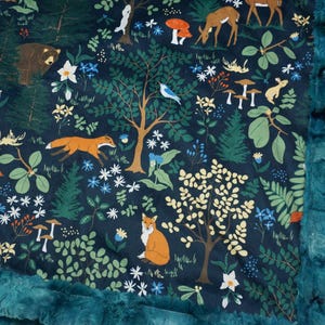 May include: A teal blue minky baby blanket with a woodland animal print. The print features foxes, bears, deer, birds, mushrooms, and flowers on a dark blue background.