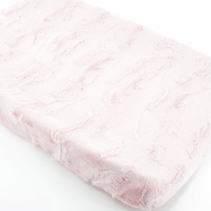 May include: A soft pink changing pad cover with a faux fur texture.