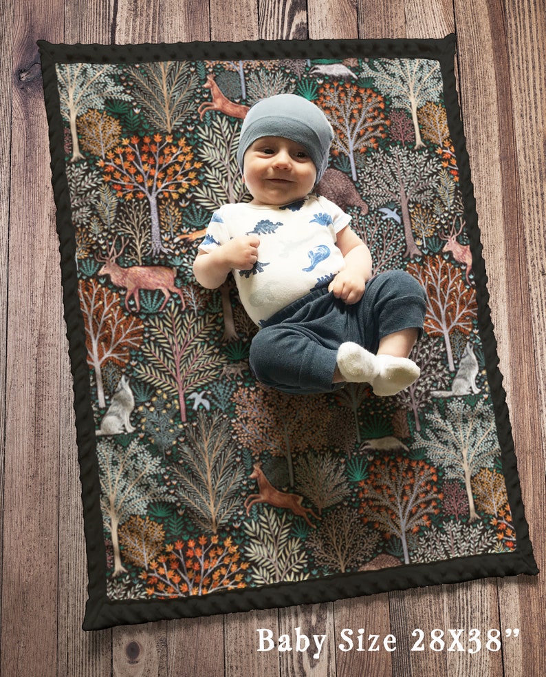 May include: A baby blanket with a woodland theme. The blanket features a dark background with colorful trees, animals, and flowers. The blanket is 28 inches by 38 inches.