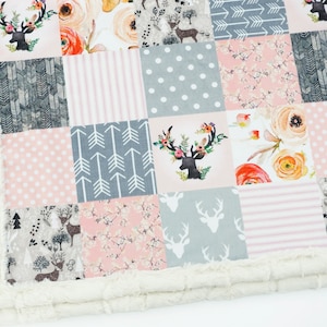 May include: A pink and grey patchwork baby blanket with a deer and floral print. The blanket has a white faux fur trim.