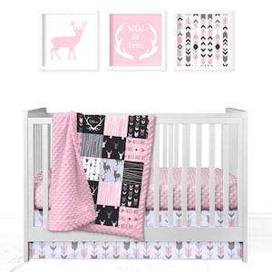 Peut inclure: Un ensemble de literie de berceau rose et gris avec une courtepointe en patchwork représentant des cerfs, des flèches et le texte "Wild and Free".