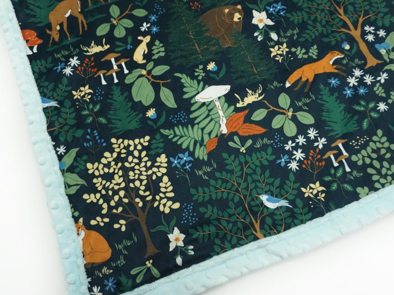 May include: A dark blue fabric with a woodland pattern featuring a variety of animals, plants, and mushrooms. The fabric has a light blue fuzzy trim.