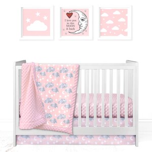 May include: Pink and gray baby crib bedding set with a cloud and star pattern. The set includes a fitted sheet, a crib skirt, and a blanket. The blanket has a soft, textured surface. The crib skirt has a ruffle trim. The set is decorated with clouds, stars, and a crescent moon.