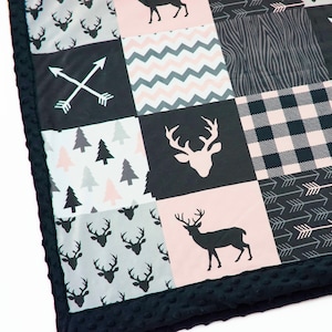 Puede incluir: Una manta de bebé negra y rosa con un diseño de patchwork que presenta ciervos, flechas, árboles y patrones de cuadros.