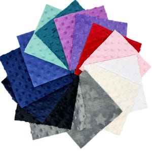Peut inclure: Une collection d'échantillons de tissu carrés disposés en éventail. Le tissu présente une texture en relief à pois dans diverses couleurs dont bleu marine, sarcelle, menthe, violet, rouge, rose, blanc, crème, noir et gris, avec un motif étoilé gris.