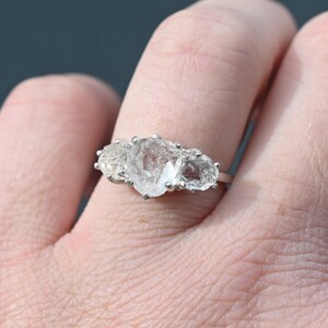 May include: A silver ring with three clear, rough-cut diamonds set in a row.
