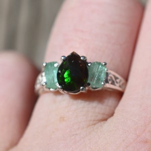 May include: A silver ring with a pear-shaped dark green gemstone surrounded by two smaller light green gemstones.