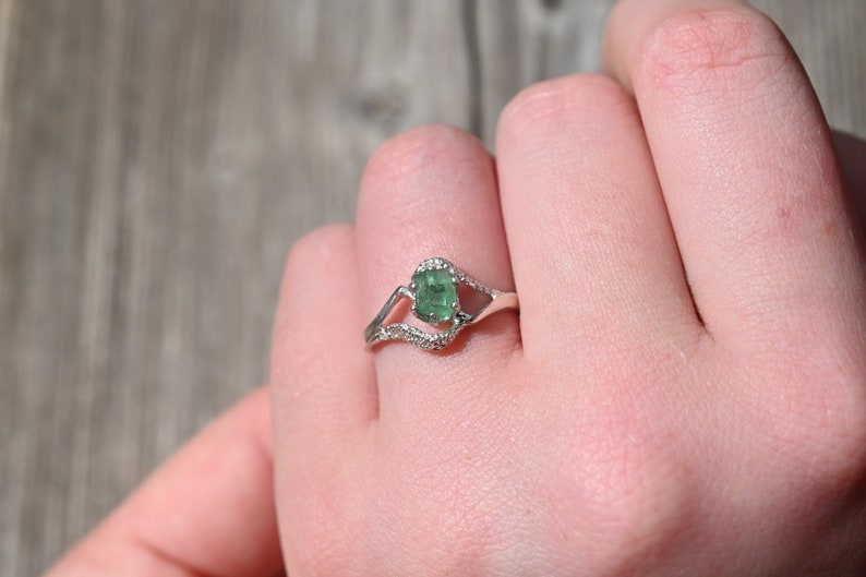 May include: A silver ring with a green gemstone and small clear stones set in a delicate design.