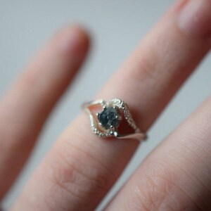 May include: A silver ring with a dark gray gemstone set in a delicate, open design.