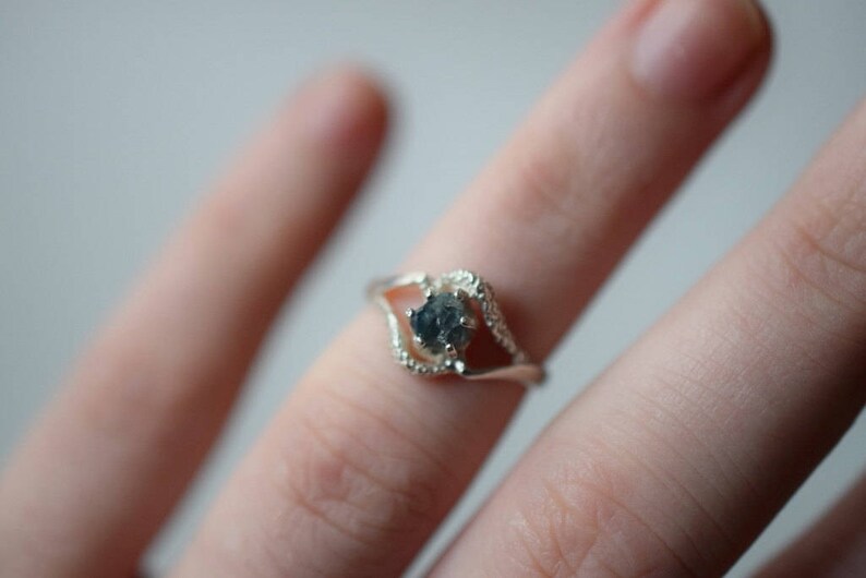 May include: A silver ring with a dark gray gemstone set in a delicate, open design.