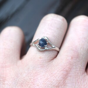 May include: A silver ring with a dark blue gemstone set in a delicate, open-work design.