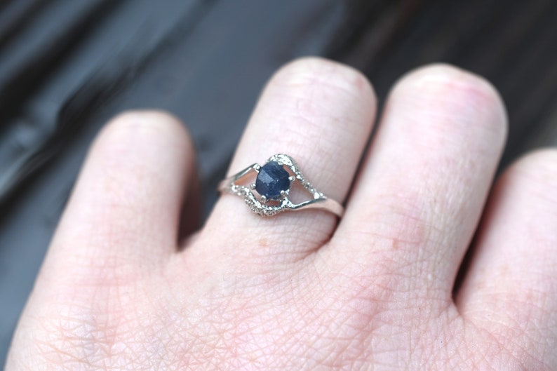 May include: A silver ring with a dark blue gemstone set in a delicate, open-work design.