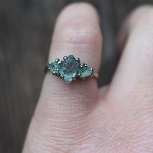 May include: A silver ring with three light blue and green gemstones set in a cluster.