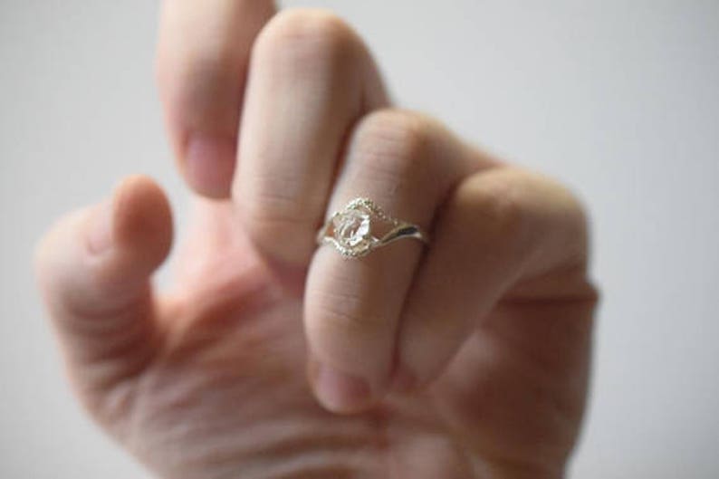 May include: A silver ring with a clear crystal stone set in a delicate, twisted band.