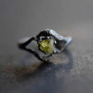 May include: A silver ring with a delicate design featuring a single, faceted, yellow-green gemstone.