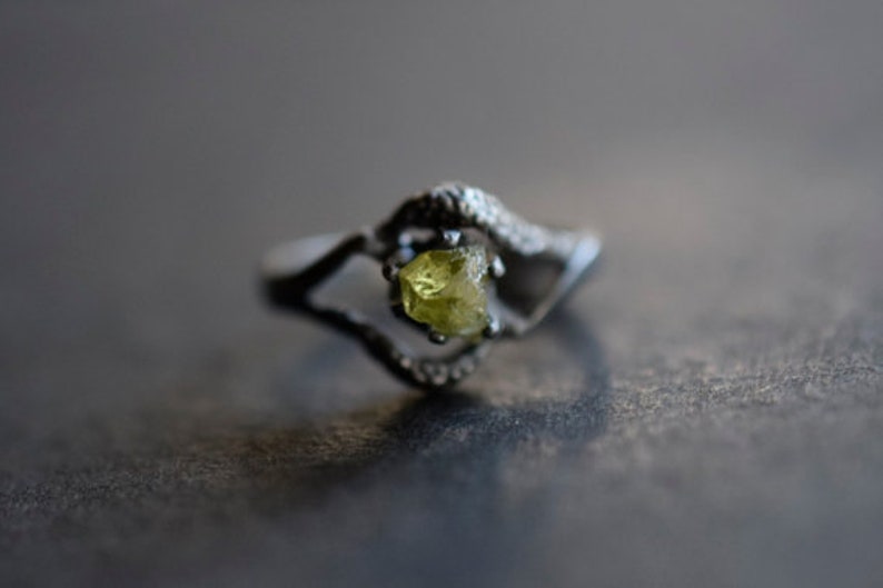 May include: A silver ring with a delicate design featuring a single, faceted, yellow-green gemstone.