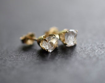 May include: A pair of gold stud earrings with clear, faceted gemstones. The gemstones are set in a simple, elegant design.