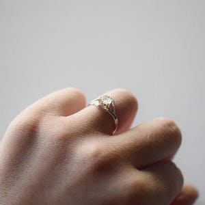 May include: A silver ring with a clear gemstone set in a delicate, twisted band.