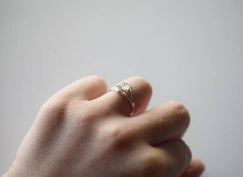 May include: A silver ring with a clear gemstone set in a delicate, twisted band.