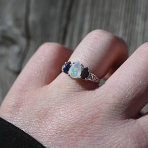 May include: A silver ring with a pear-shaped opal and three smaller pear-shaped blue sapphires.